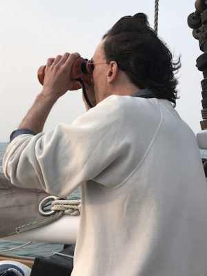 man on schooner looking through binoculars